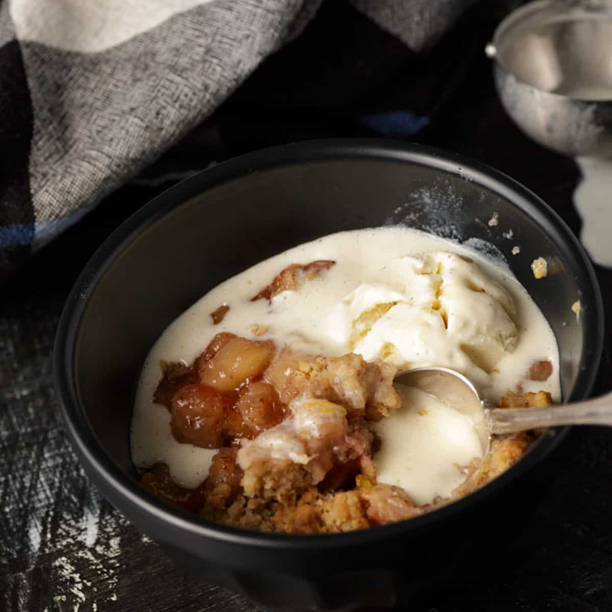 Peach and pecan crumble in a black bowl with a scoop of ice cream.