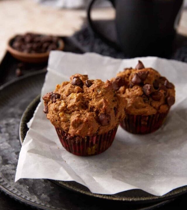 Two banana chocolate chip muffins on a plate with parchment paper.