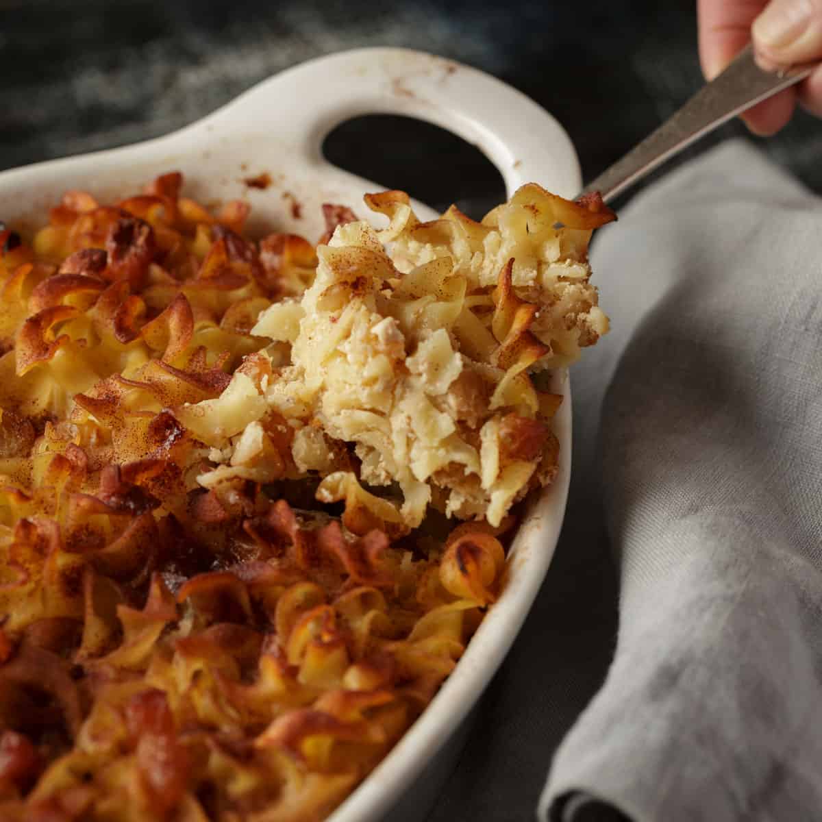 Noodle kugel in a white baking dish with a serving spoon.