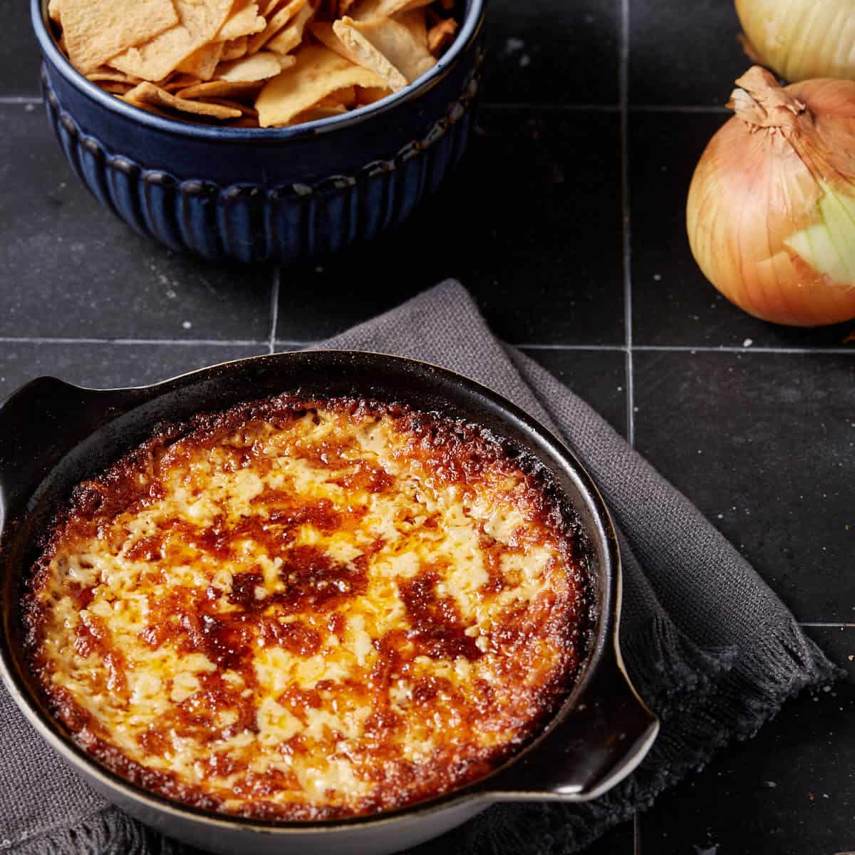 A black baking dish with cheesy vidalia onion dip, next to vidalia onions.
