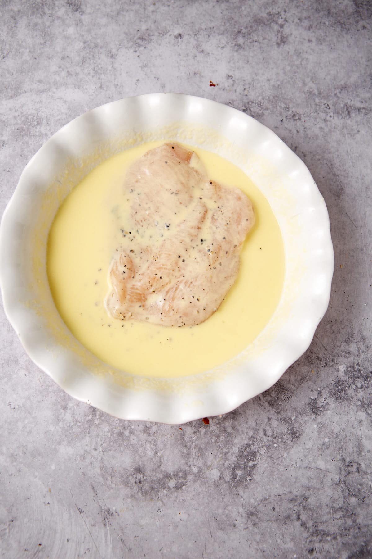 A chicken breast in a mixture of egg and buttermilk.