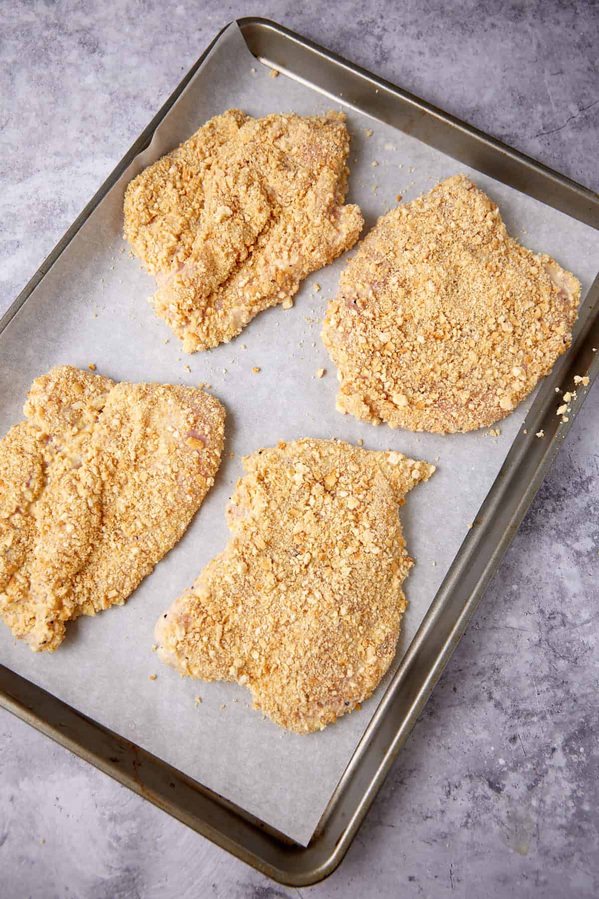 Chicken breasts coated with Ritz crackers on a baking sheet.
