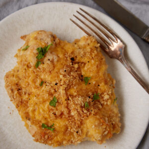 A ritz chicken breast on a plate with a fork and knife.