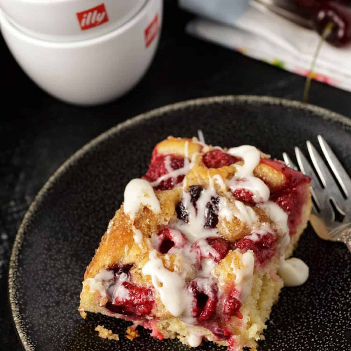 A serving of cherry and raspberry coffee cake with icing drizzled on top.