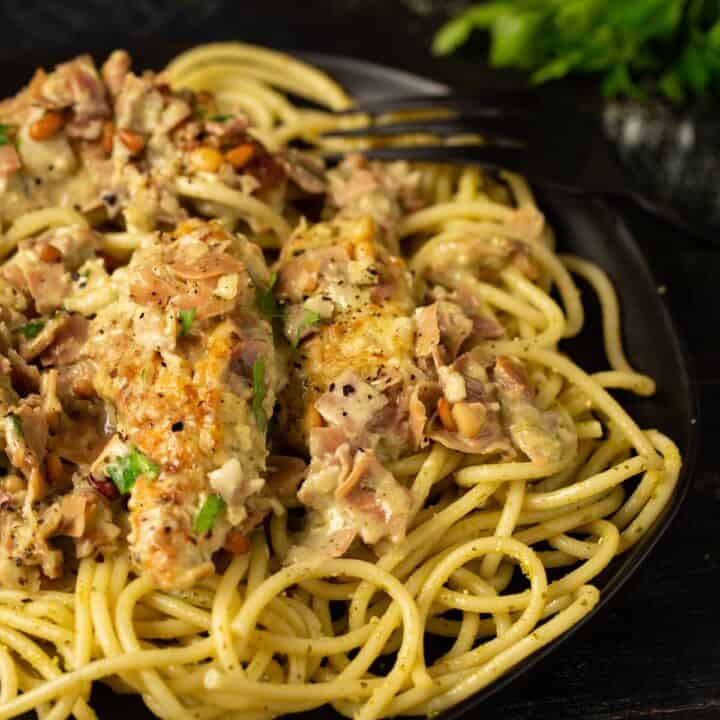 Creamy pesto chicken on a black platter over pasta.