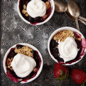 Three ramekins of strawberry rhubarb crisp topped with whipped cream.