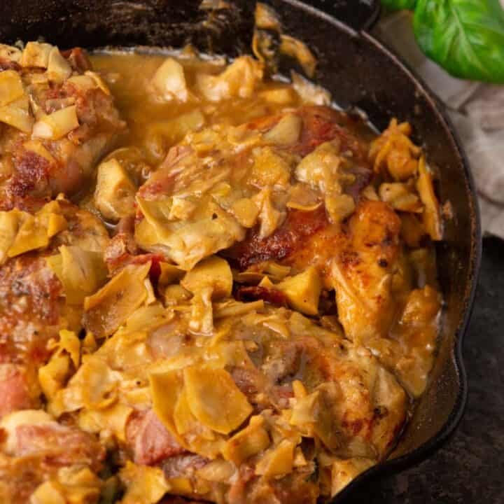 A skillet of chicken saltimbocca with basil leaves on the side