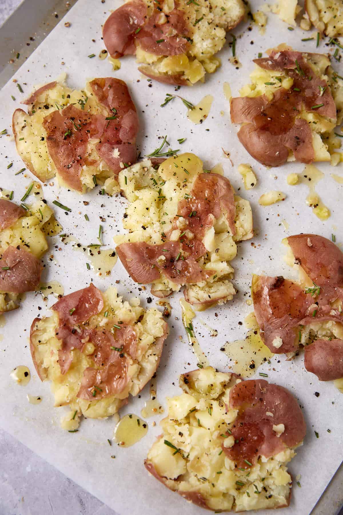 Olive oil and seasonings sprinkle over potatoes on a baking sheet.