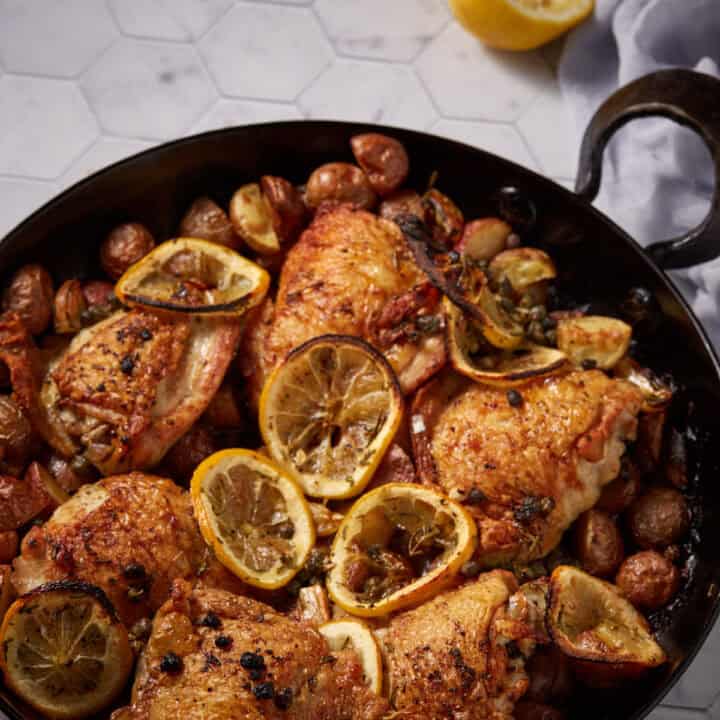 An oven proof skillet filled with roasted chicken with lemnons.