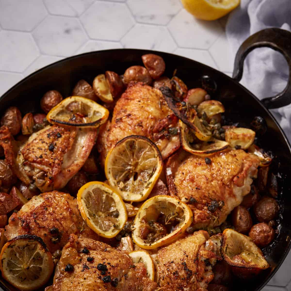 An oven proof skillet filled with roasted chicken with lemnons.