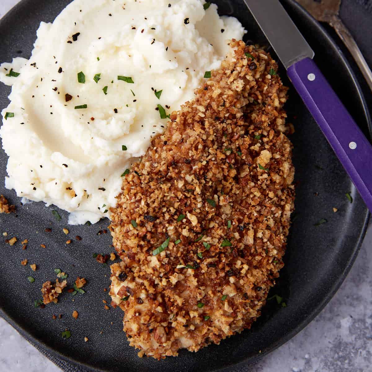 pecan crusted chicken on a black plate with mashed potatoes on the side.