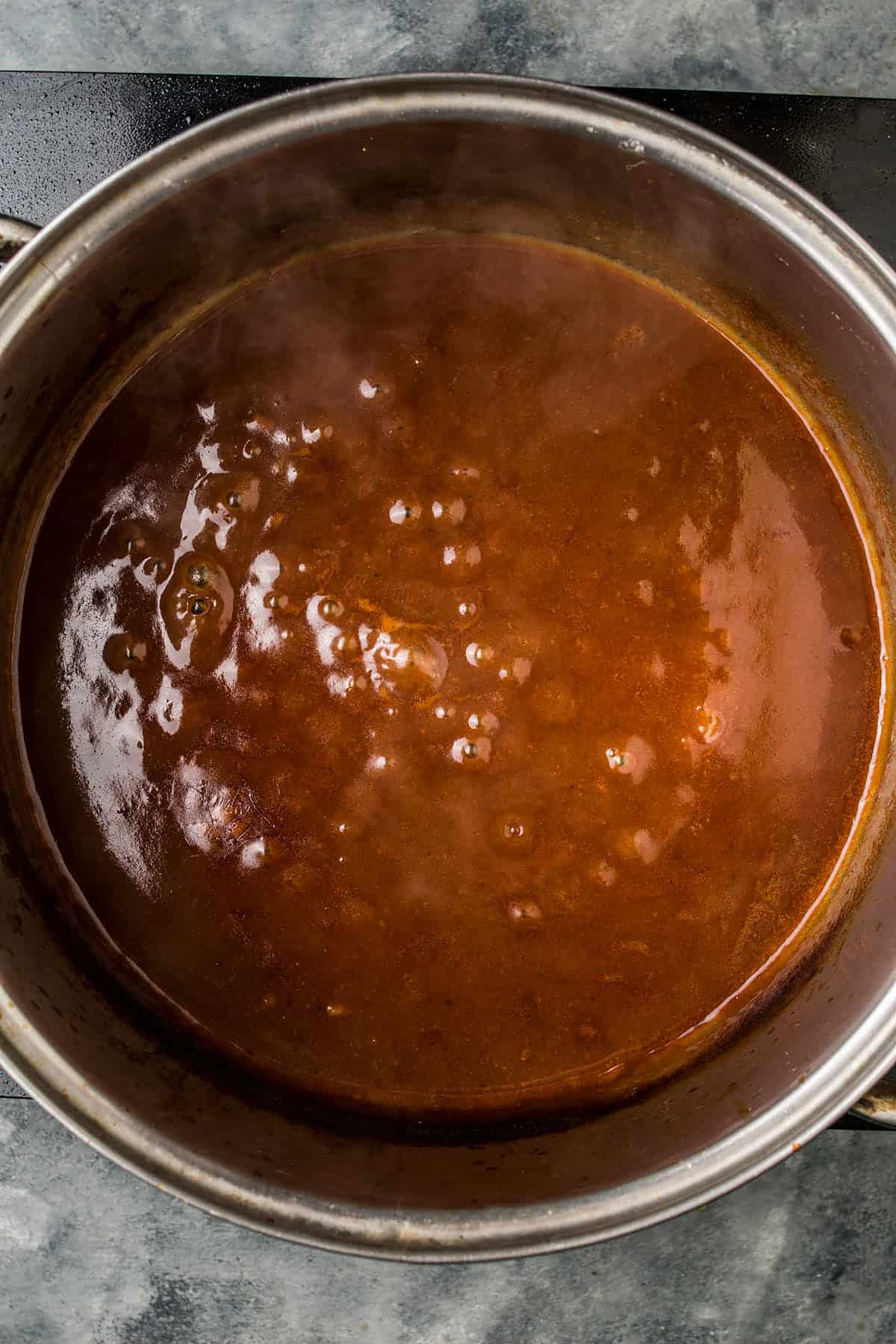 A pot of Beef Bourguignon simmers on the stovetop, its rich, reddish-brown sauce bubbling gently as aromatic steam drifts into the air.