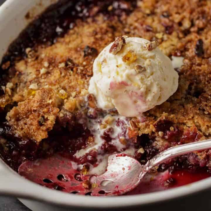 A serving spoon in a baking dish of blackberry crumble.