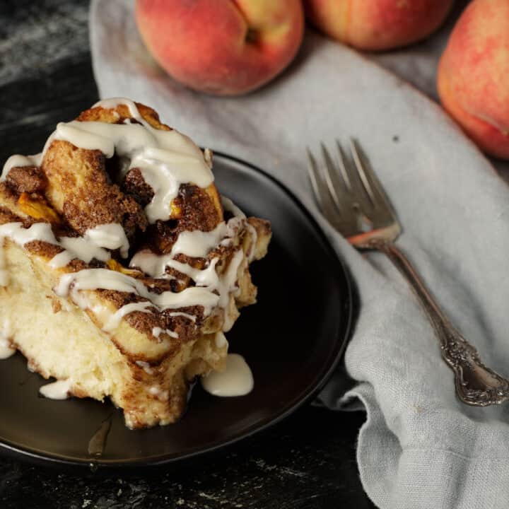 A peach cinnamon roll on a black plate.