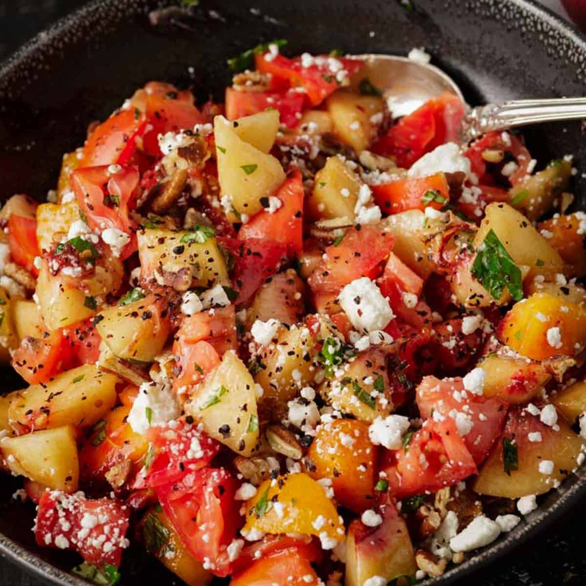 A bowl of fresh peach and tomato salad with a spoon.