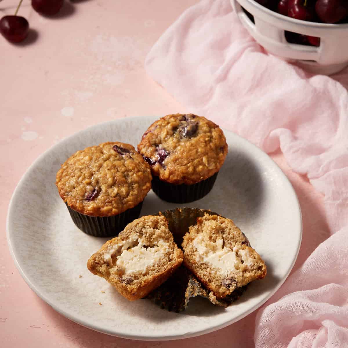 Cherry oatmeal muffins cut open with a cheesecake filling on a plate.