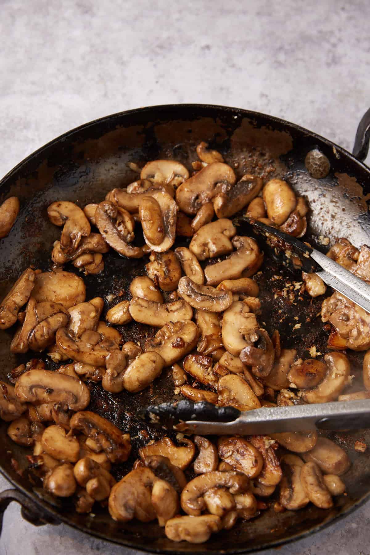 mushrooms being sautéed in a skillet with tongs.