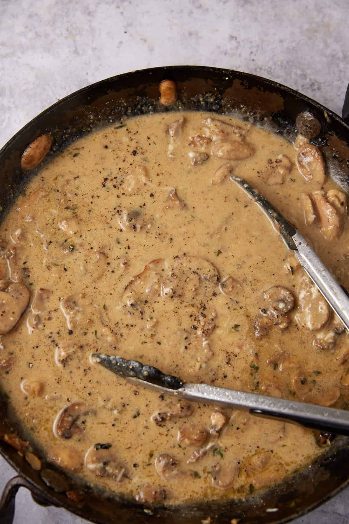cream added to the sautéed mushroom mixture in a skillet with tongs.