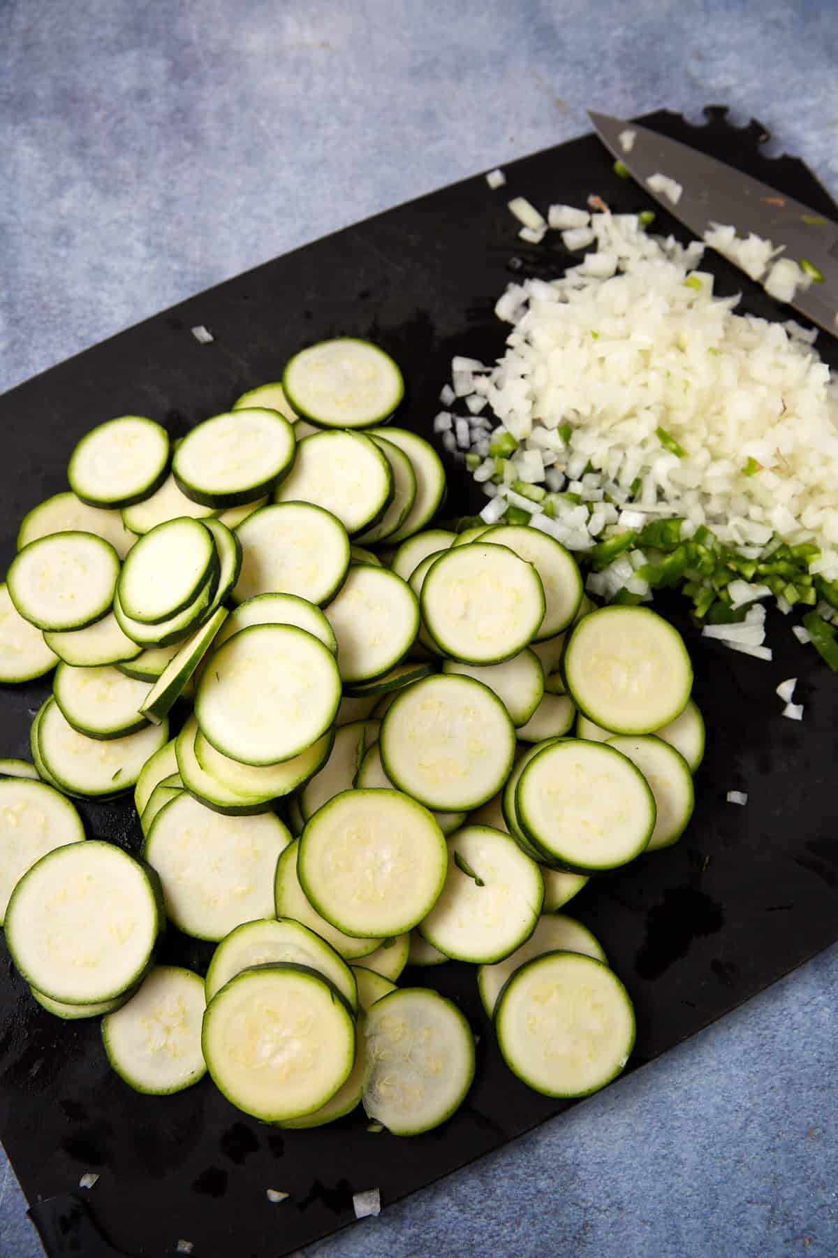 Sliced squash and chopped onions and peppers on a cutting board.