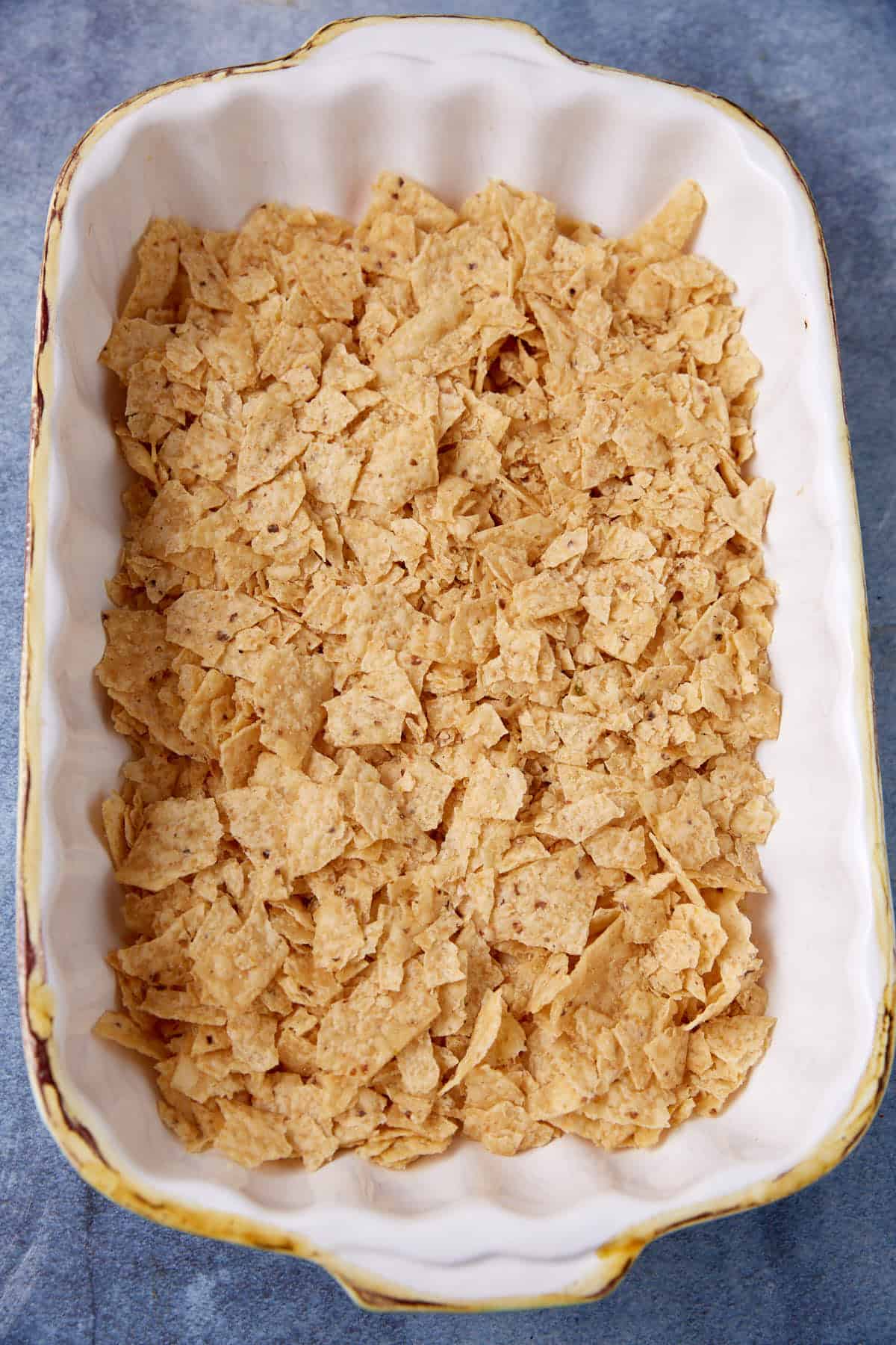 Tortilla chips crumbled on the bottom of a casserole dish.