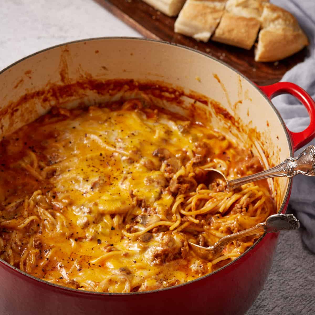 A red pot full of spaghetti casserole with two serving spoons.