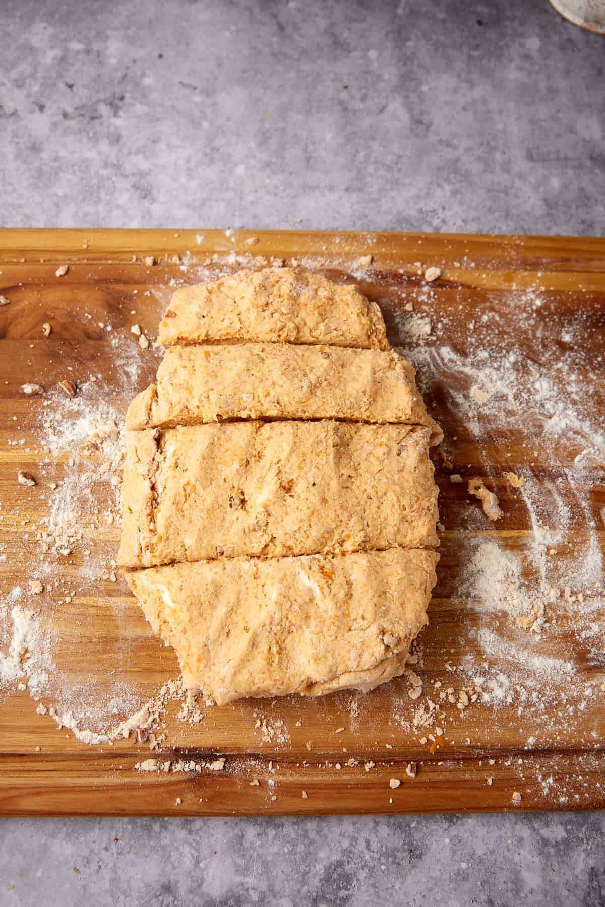 A slab of biscuit dough on a floured wooden surface, cut into four rectangular pieces, ready to be baked for an Apple Cobbler with Sweet Potato Biscuits.