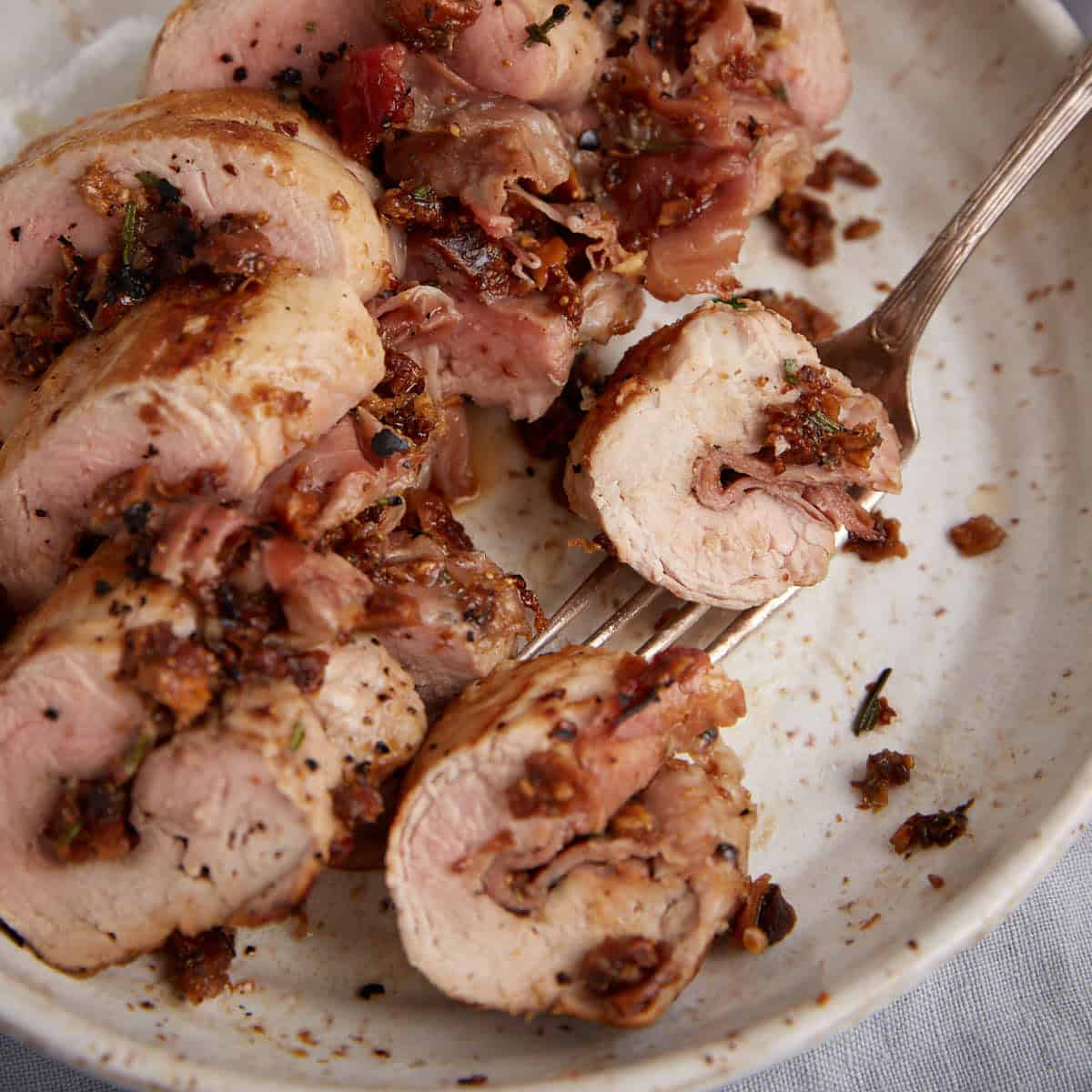 A platter of stuffed pork tenderloin with a serving spoon.