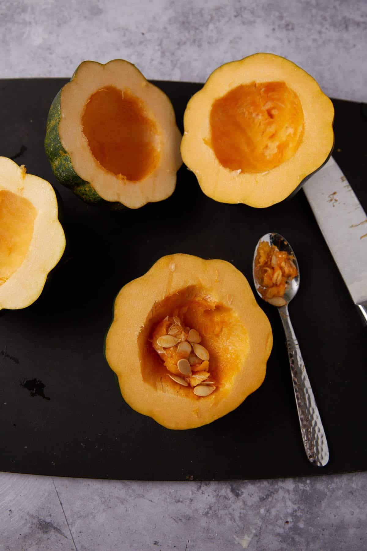 seeds being stopped out of acorn squash halves on a cutting board.