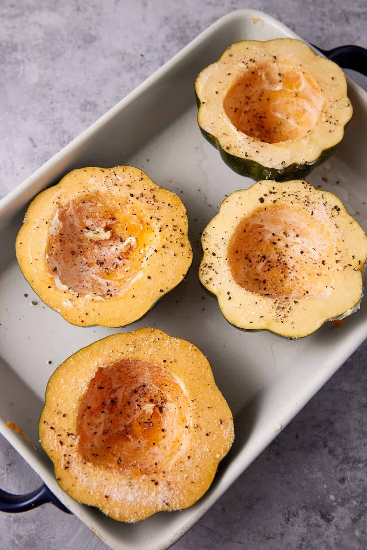 acorn squash halves sprinkled with salt, pepper, and oil in a baking dish.