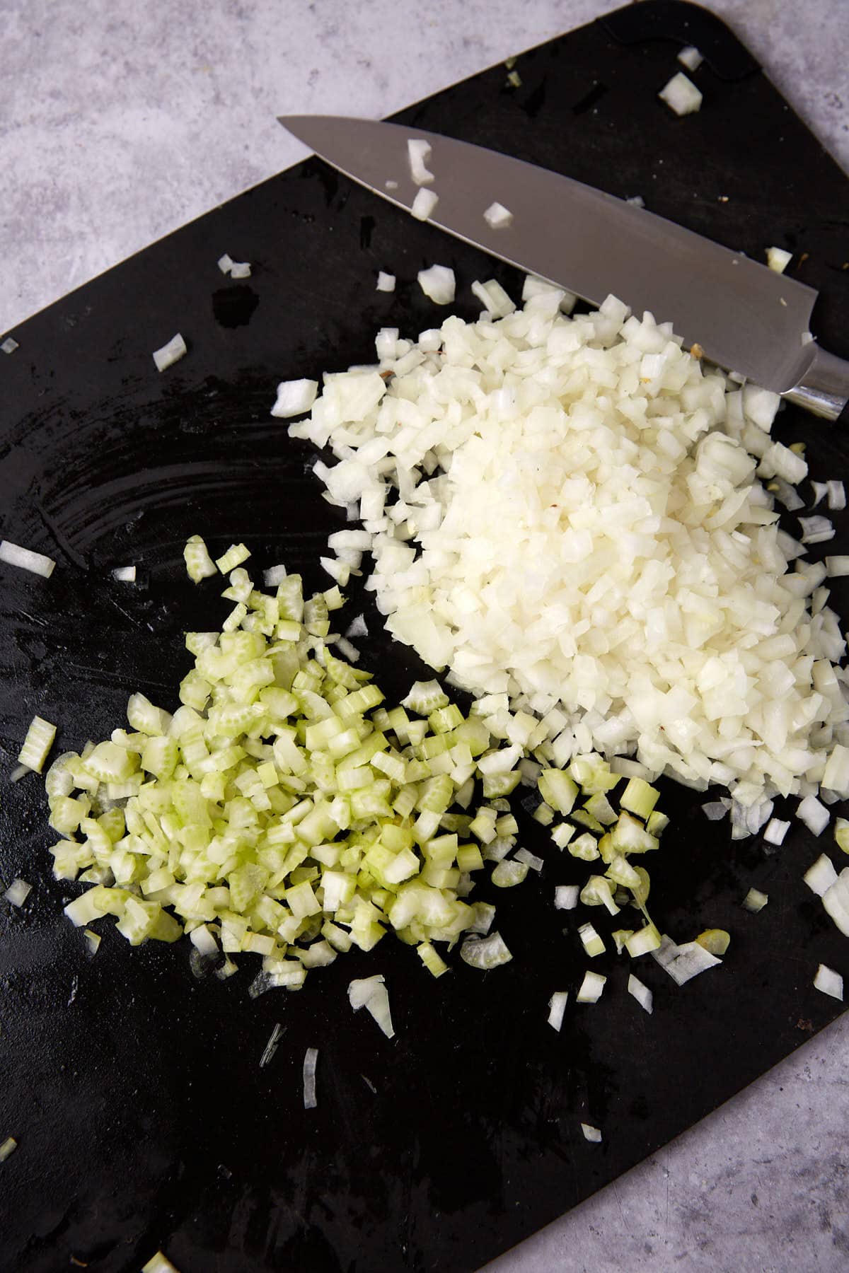 chopped onions and celery on a cutting board with a knife.