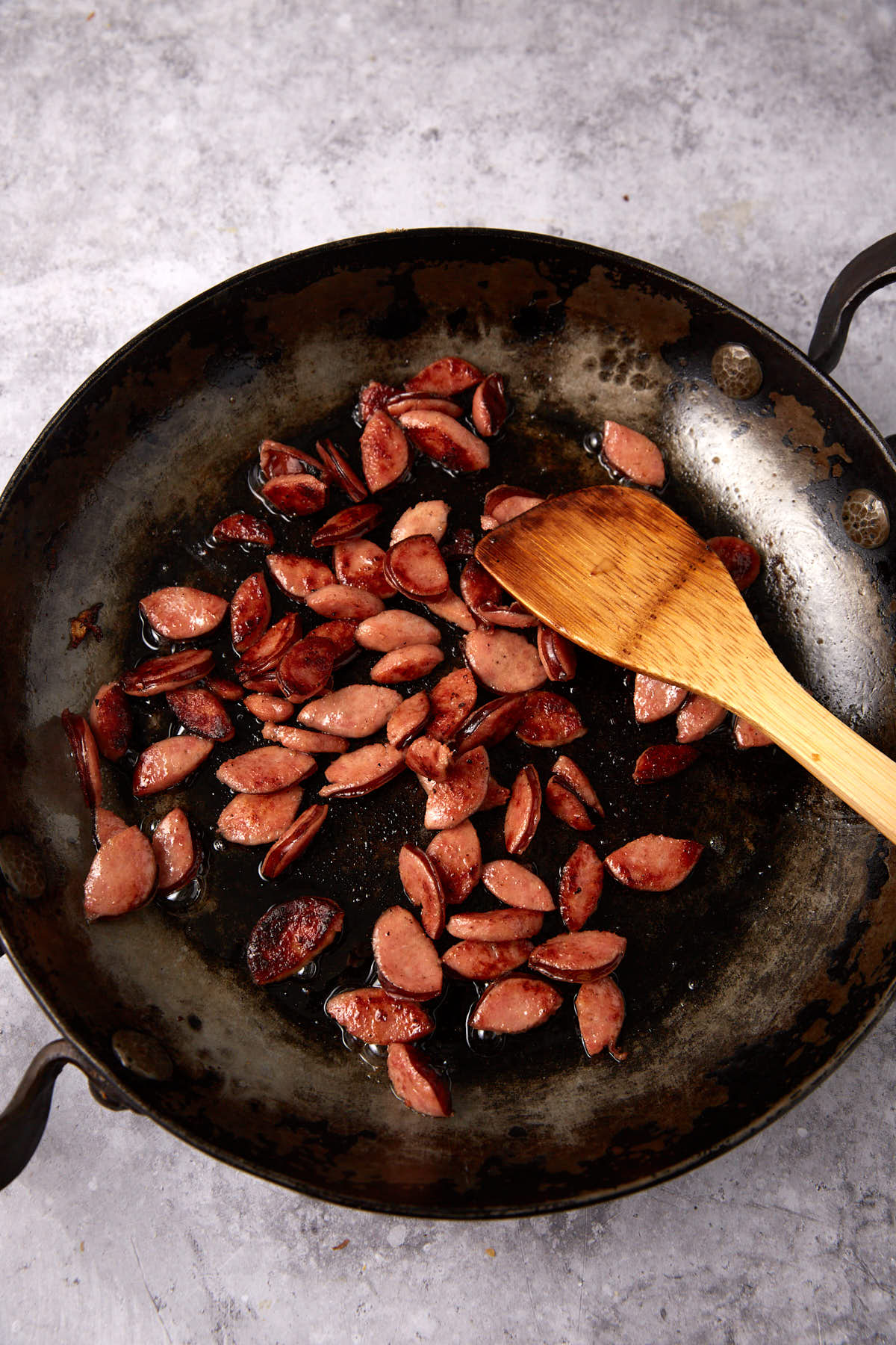 sautéed sausage in a skillet with a wooden spoon.