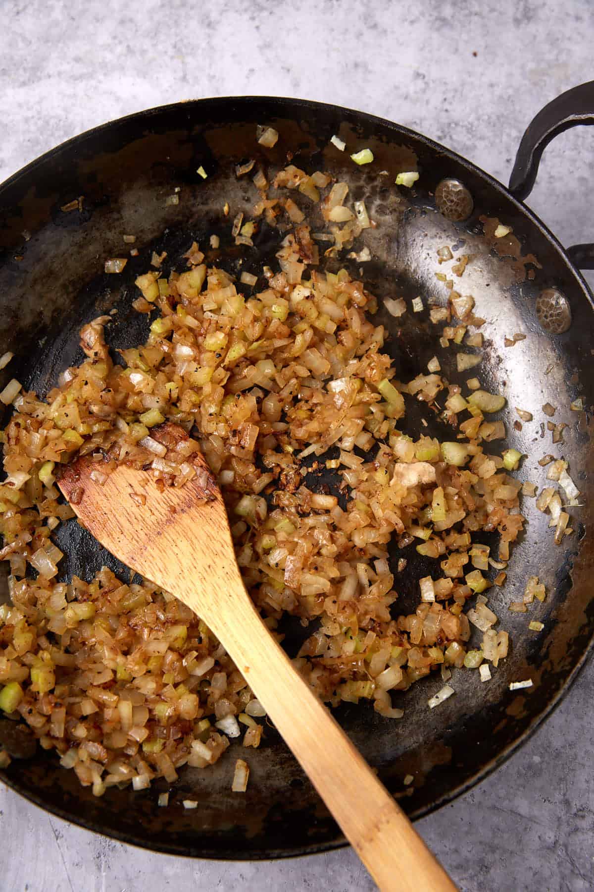 sautéed onions and celery in a skillet with a wooden spoon.