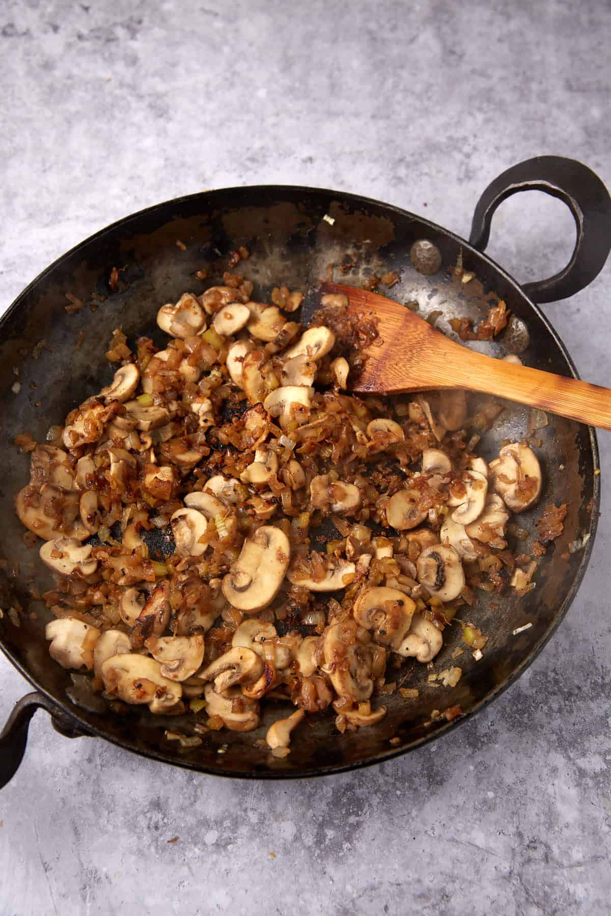 sauteed celery, onions, and mushrooms in a skillet with a wooden spoon.