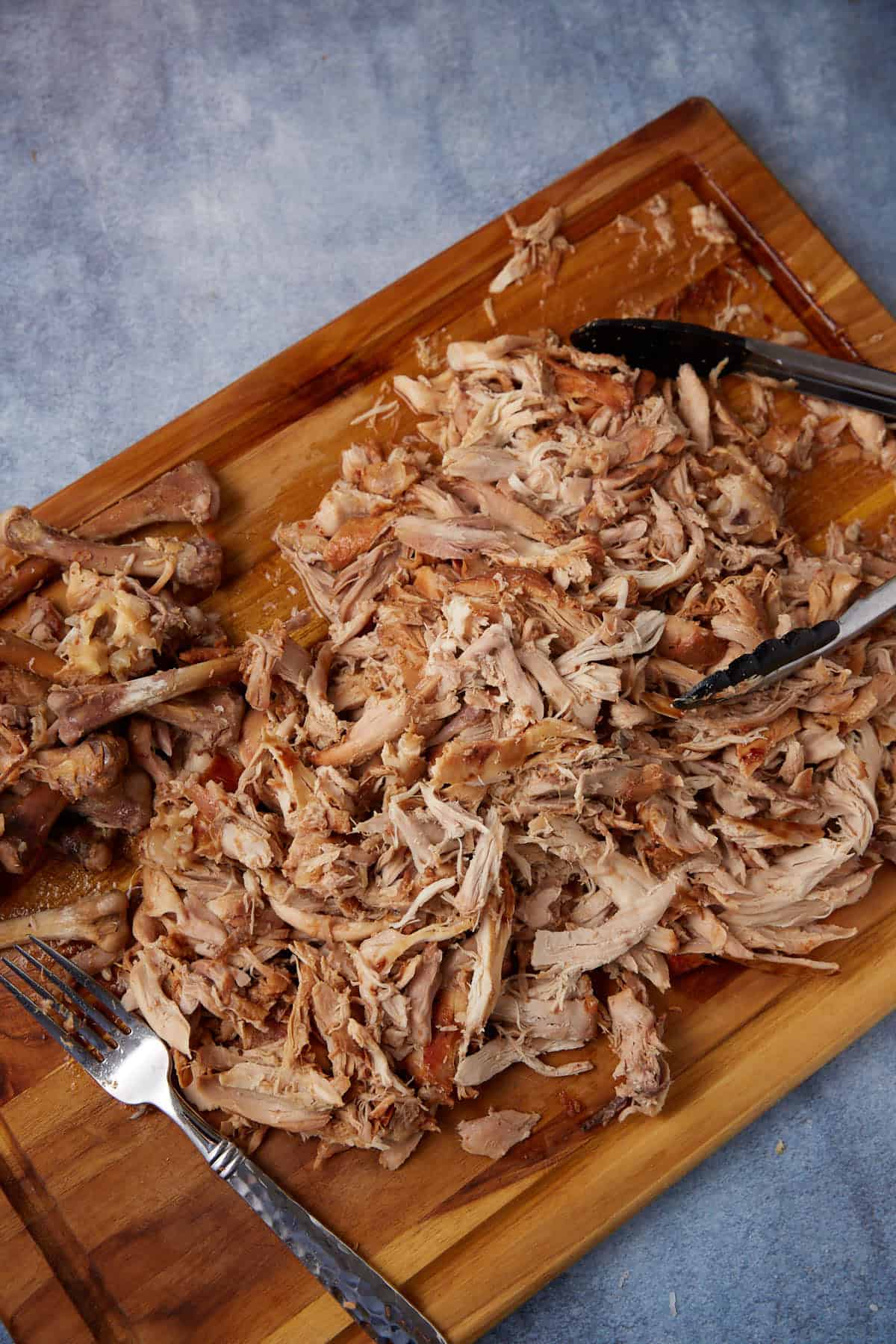Shredded chicken with a fork on a cutting board.