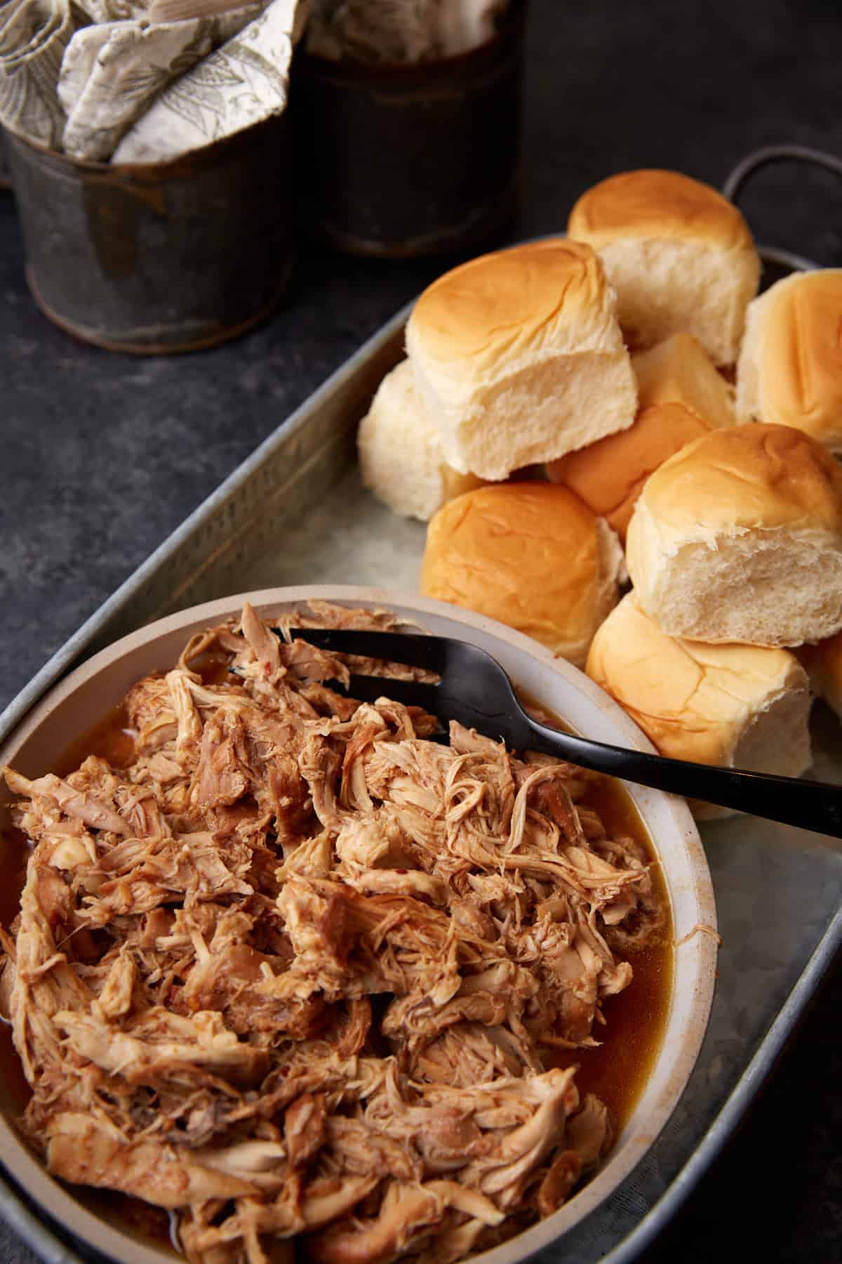 bbq pulled chicken in a bowl next to rolls.