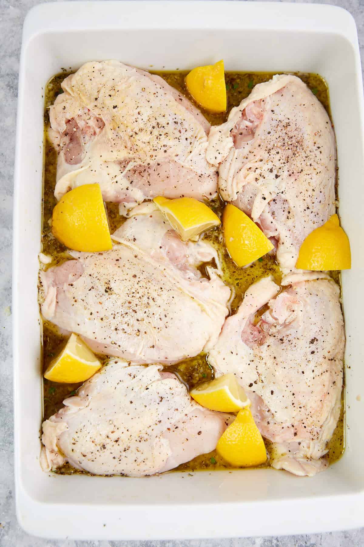 Chicken in a baking dish with lemon wedges.