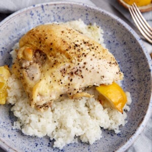 A baked chicken breast on a bed of rice with lemon wedges.