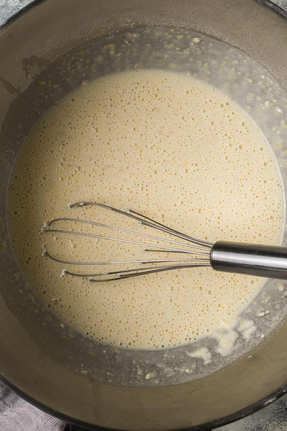 A metal whisk rests in a mixing bowl filled with pale, frothy batter—perfect for making delicious blueberry pancakes.