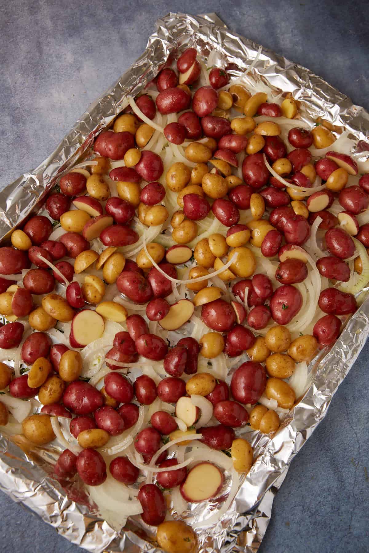 Cut potatoes and sliced onions on a foil lined baking sheet.