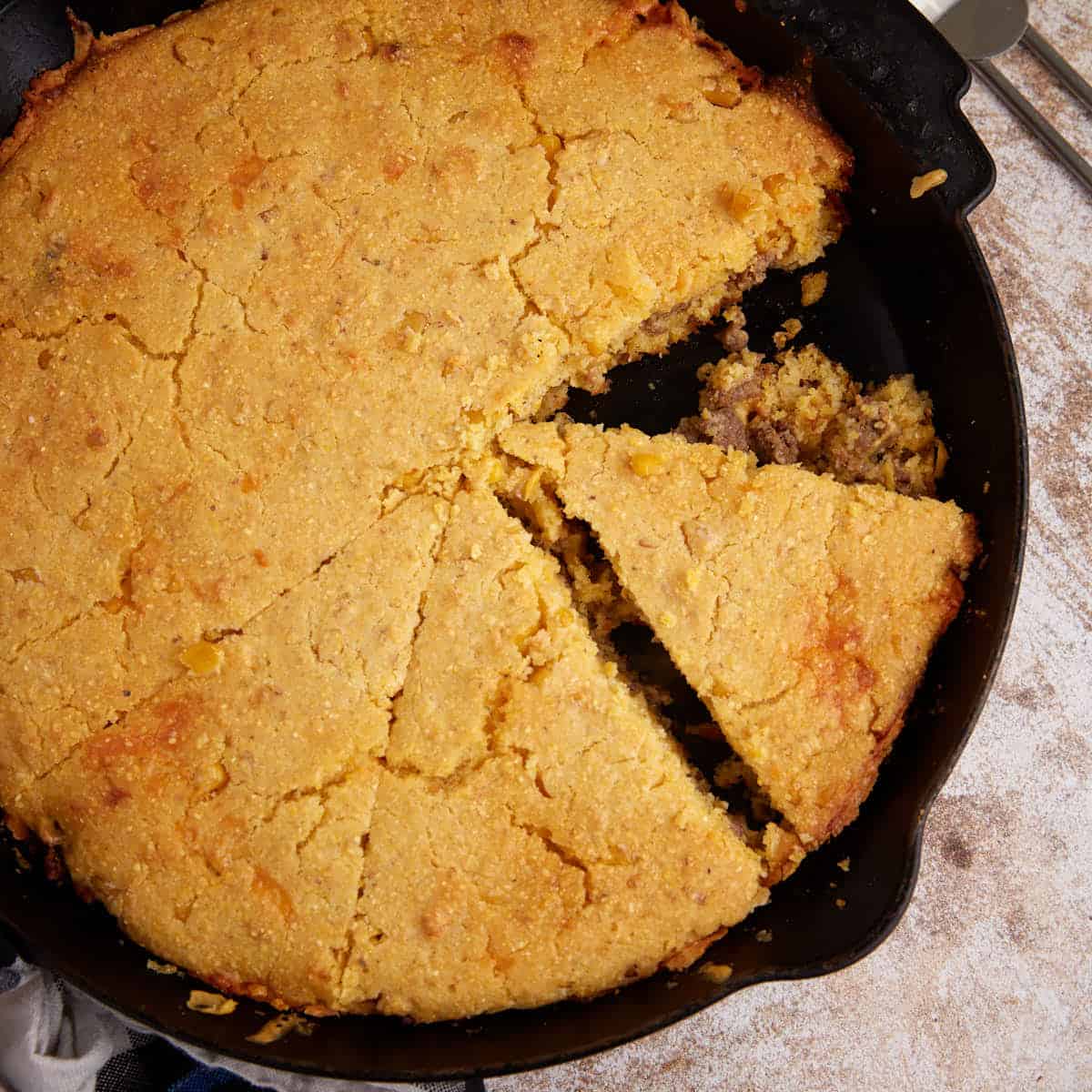 A skillet of sausage cornbread that has been sliced.