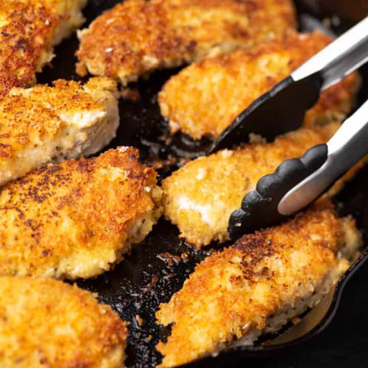 Tender chicken strips coated with panko and parmesan in a skillet.