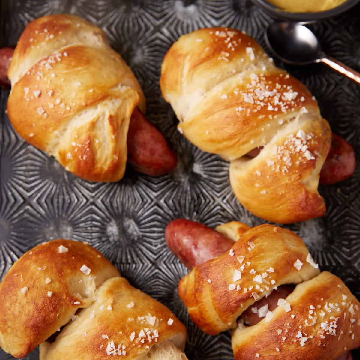 Pretzel wrapped bratwurst on a platter.