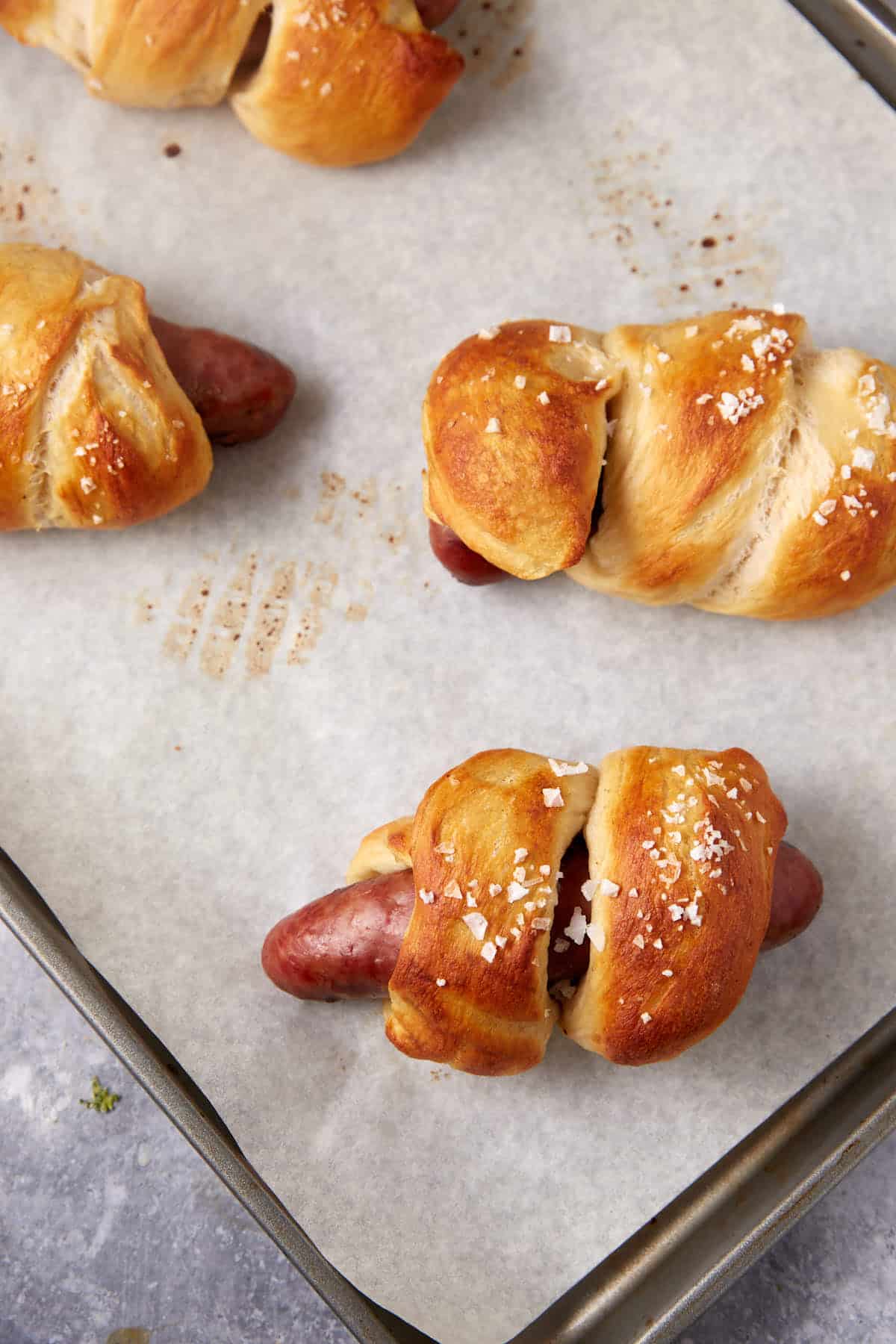 Baked pretzel wrapped brats on a baking sheet.