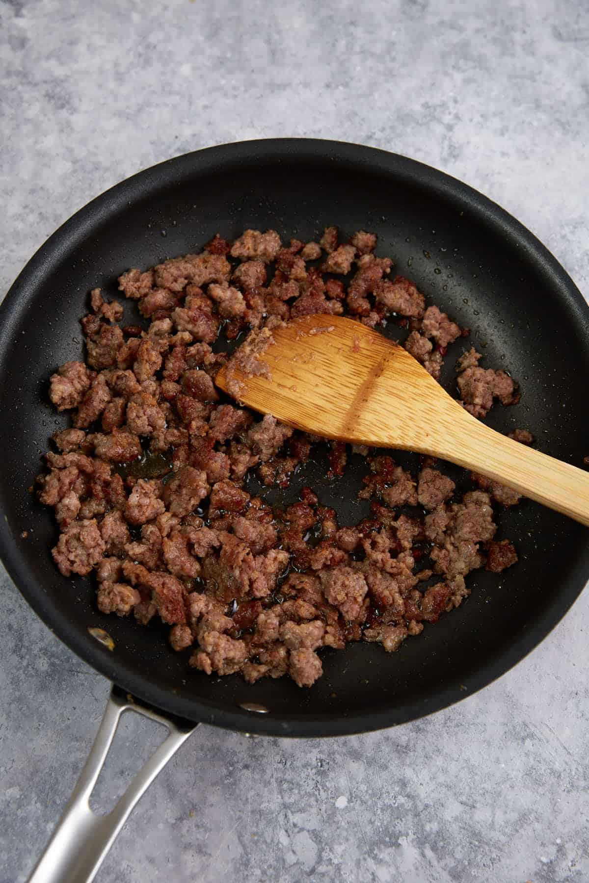 Sausage cooked in a skillet with a wooden spoon.