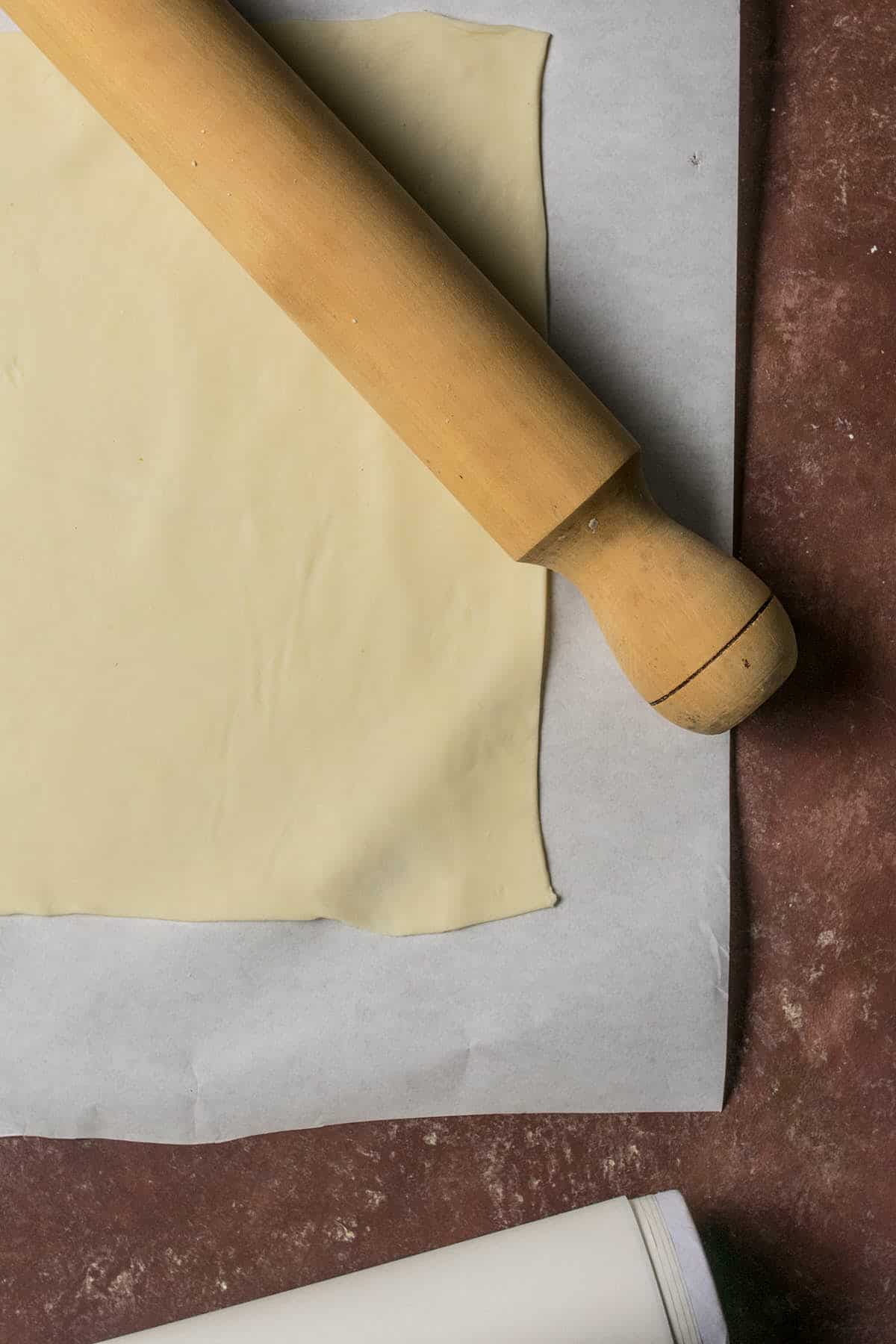 A rolling pin rests on a sheet of parchment paper with rolled-out dough, ready to be transformed into a delicious Goat Cheese and Fig Tart, set on a brown surface.