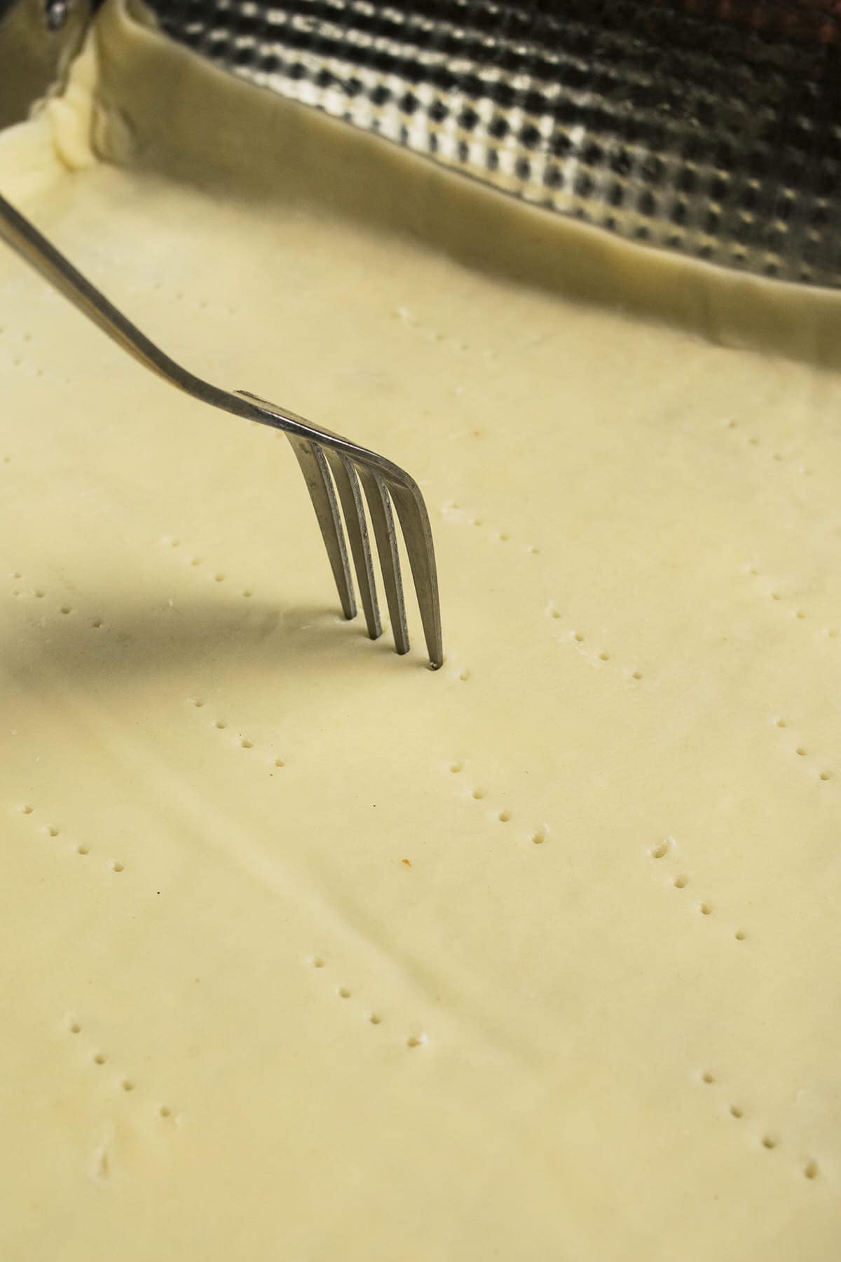 A close-up of a fork pricking holes in an unbaked Goat Cheese and Fig Tart crust dough in a baking pan.