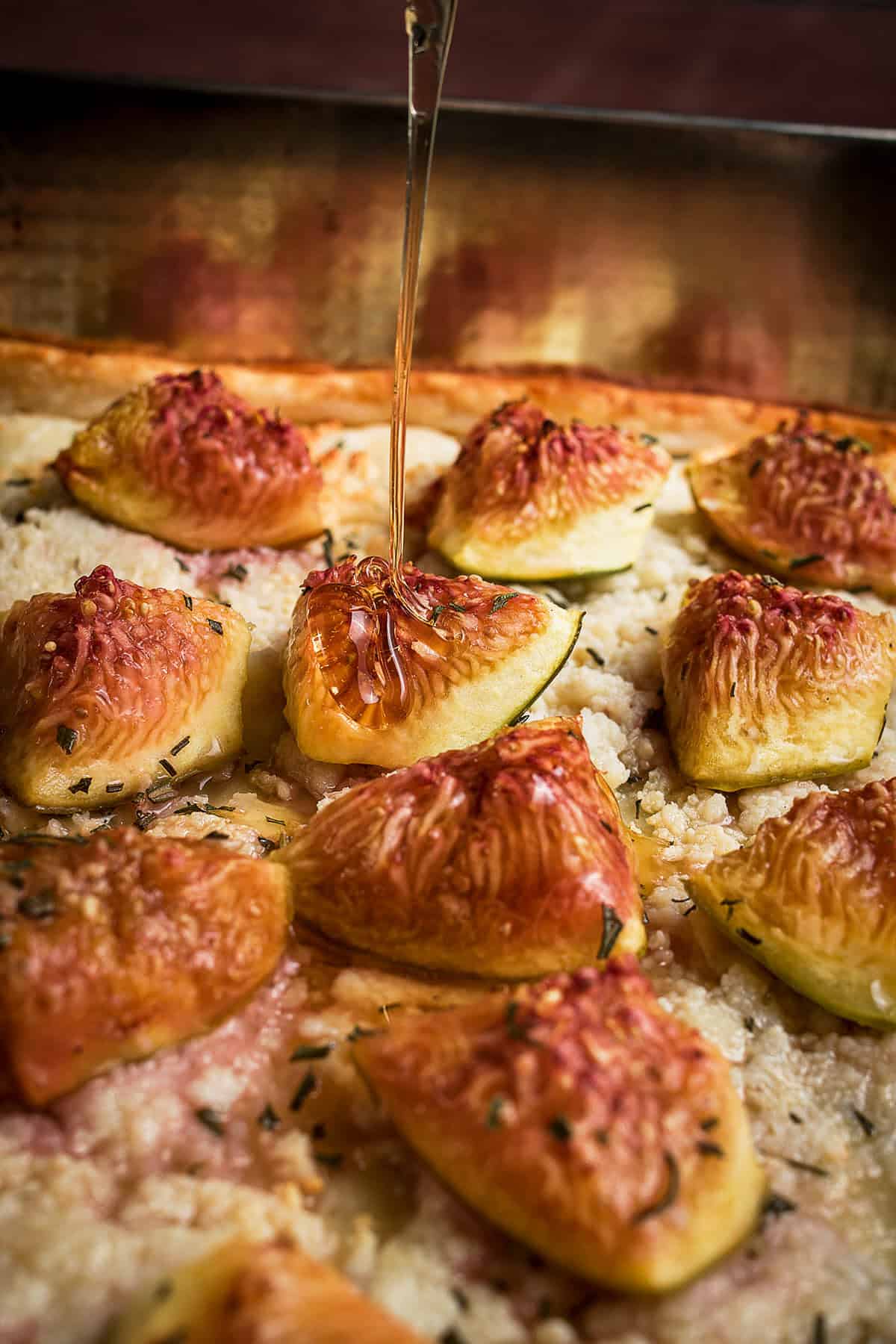 Close-up of a Goat Cheese and Fig Tart pizza topped with sliced figs and herbs, with honey being drizzled over it. The golden crust and melted cheese create an irresistible savory and sweet combination.
