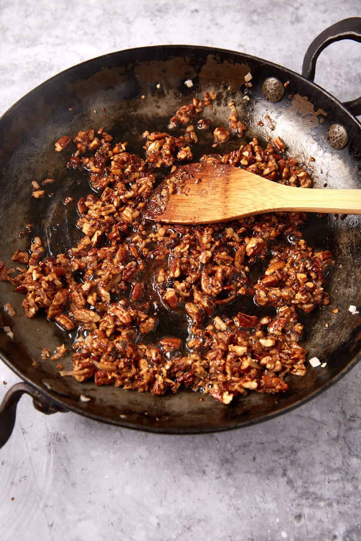 toasted pecans, shallots, and maple syrup in a black skillet with a wooden spoon.