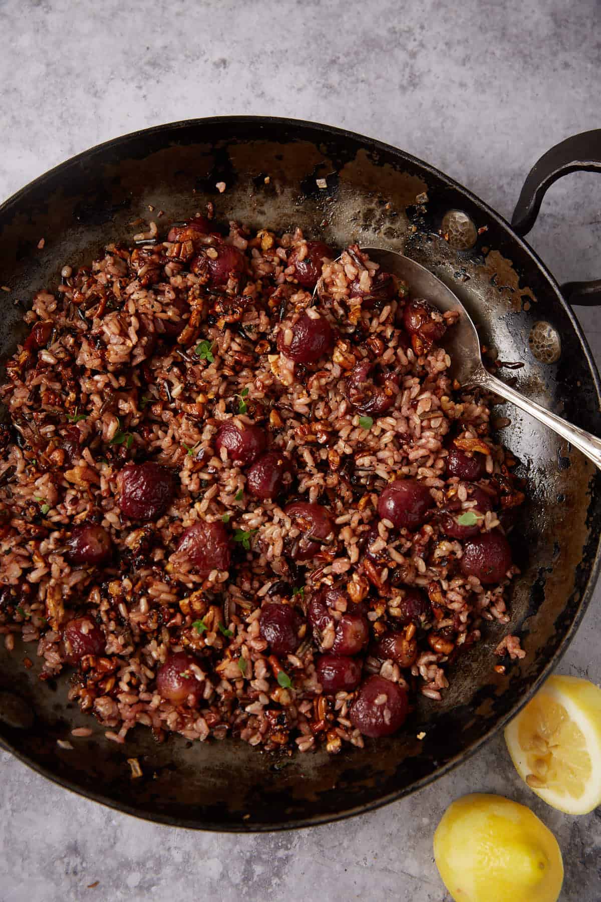 wild rice with grapes in a skillet being stirred with a spoon.