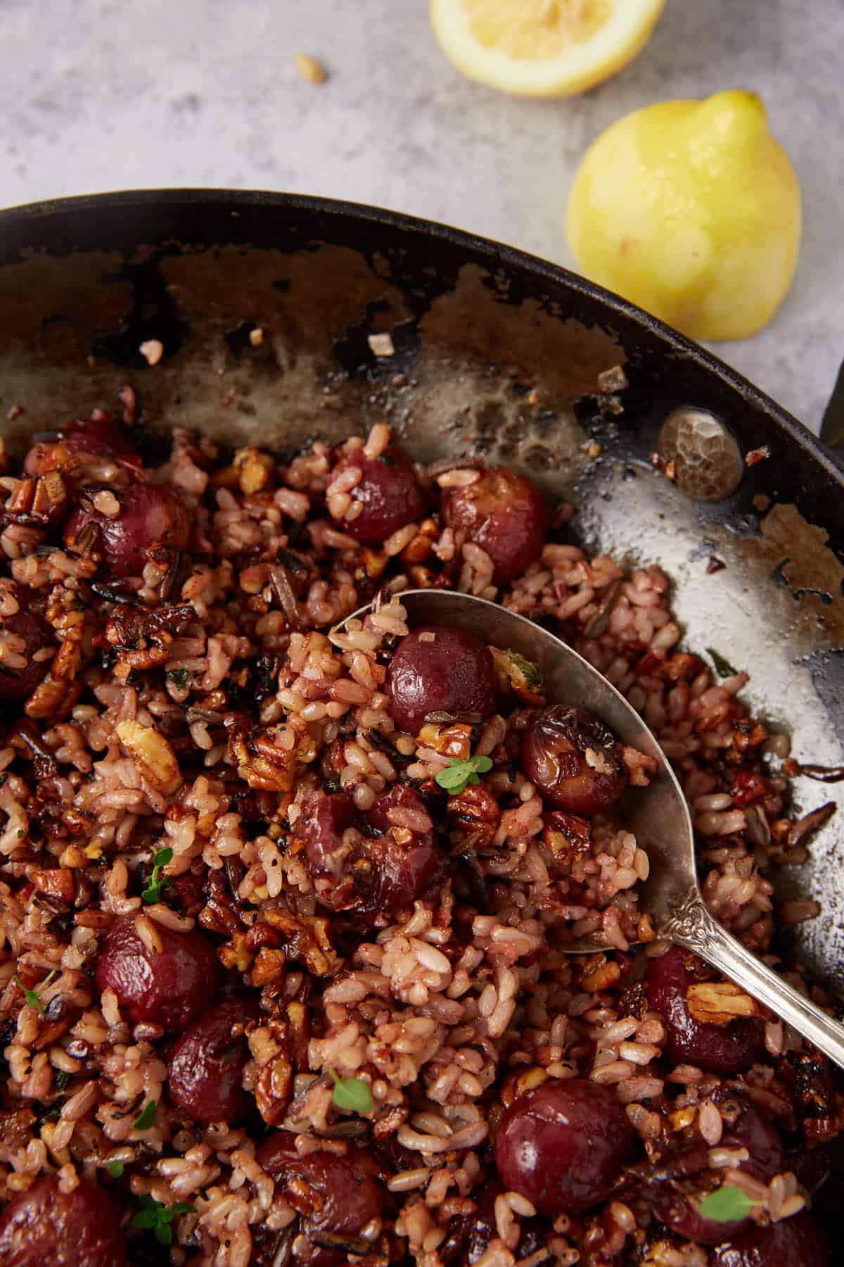 wild rice with grapes in a skillet being stirred with a spoon.
